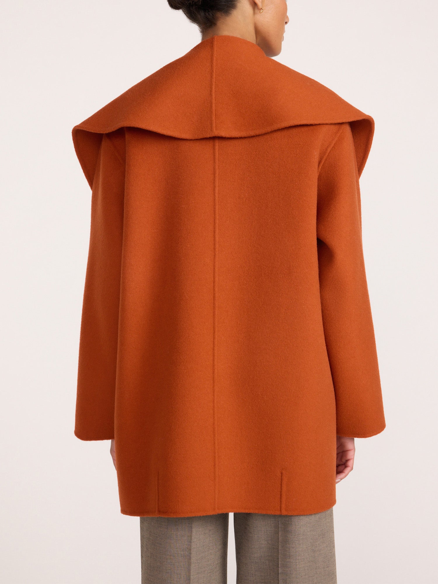 Oversized wrap coat in rust orange, back view with dramatic wide collar over gray trousers