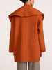 Oversized wrap coat in rust orange, back view with dramatic wide collar over gray trousers