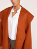 Close-up of the oversized wrap coat in rust orange, draped over a white button-down shirt and gray trousers