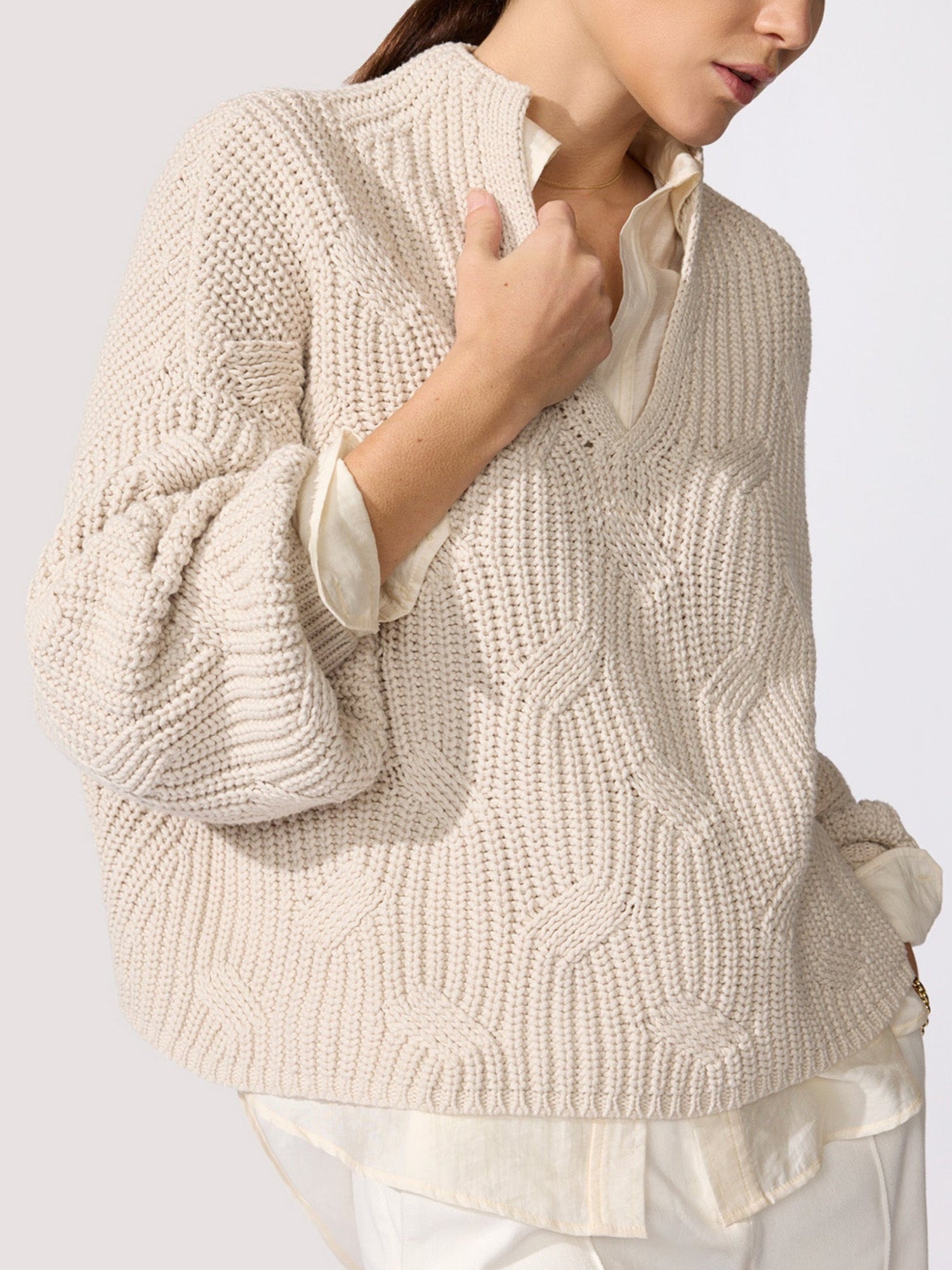 Classy women's sweater in oatmeal chunky cable knit with a V-neckline and balloon sleeves layered over a cream shirt shown in close-up.