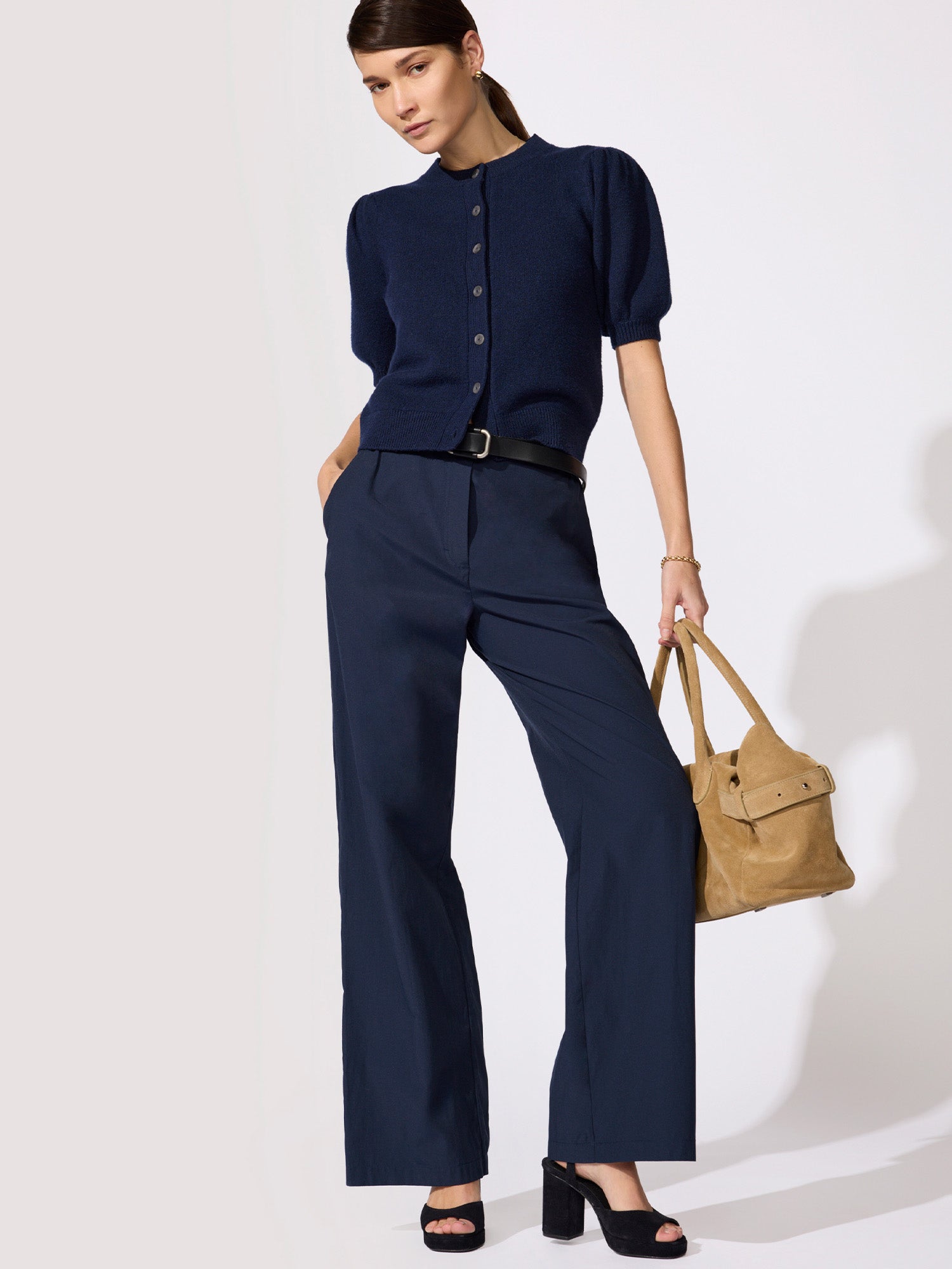 Classy navy blue outfit with a puff-sleeve button-front cardigan and matching wide-leg trousers with a black belt and tan suede tote bag.