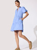 Woman wearing a periwinkle blue tiered ruffle mini shirtdress with puff sleeves and front pockets, styled with tan loafers.