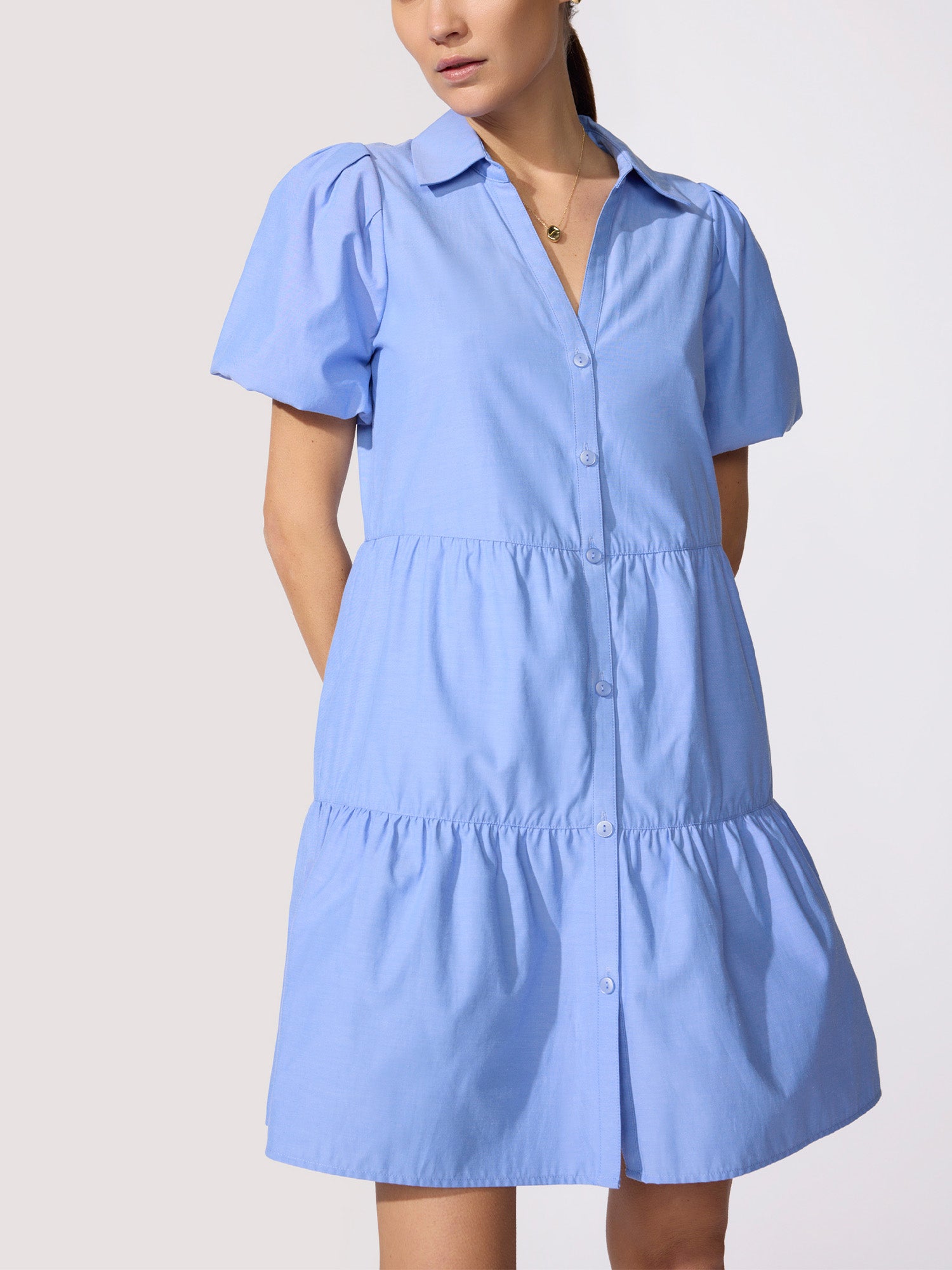 Close-up of a periwinkle blue mini shirtdress with puff sleeves, button-front placket, and tiered ruffle skirt on a model.