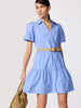 Woman in a periwinkle blue belted mini shirtdress with puff sleeves and a tiered ruffle hem, carrying a tan suede tote.