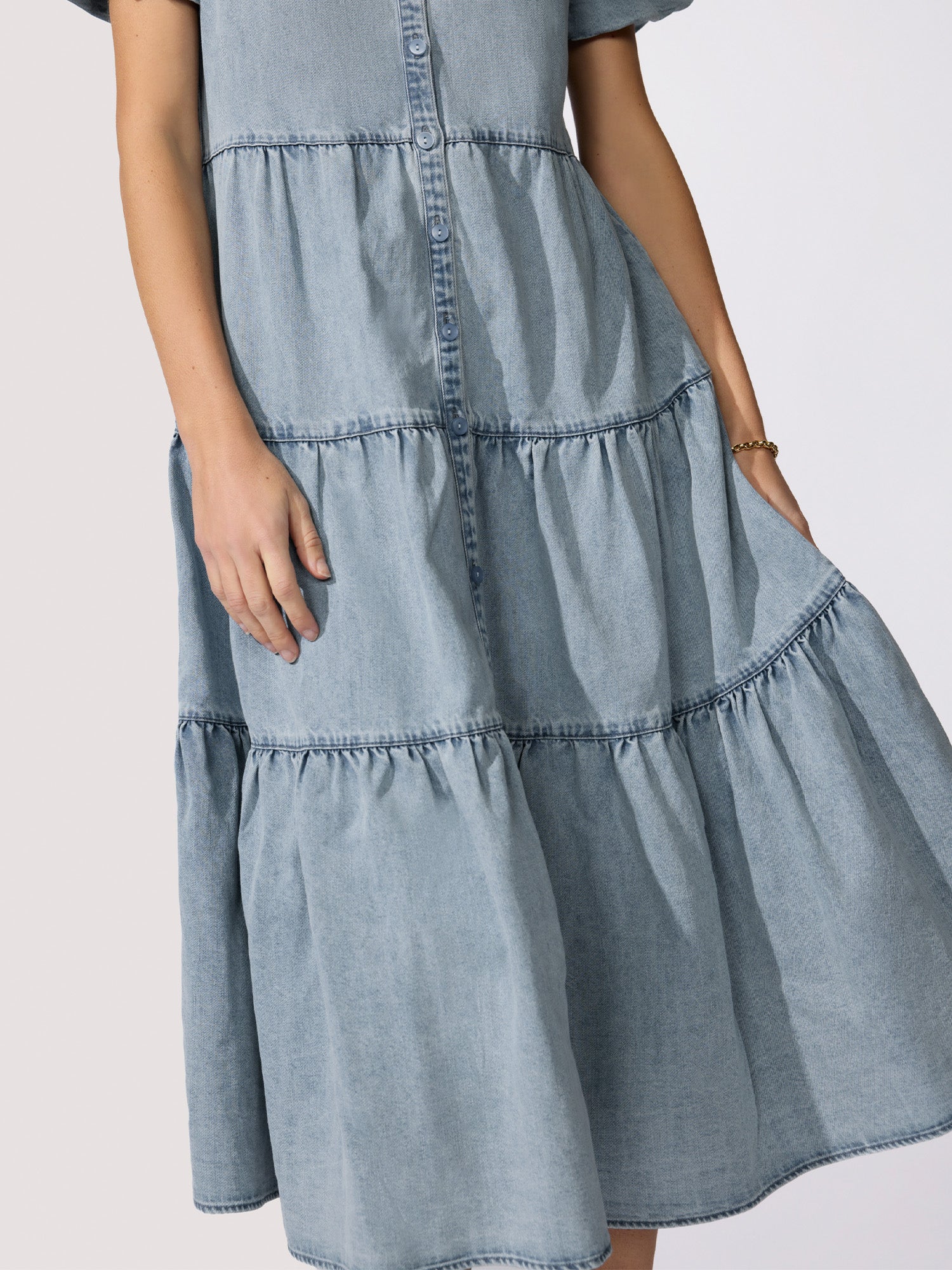 Simple classy dress in light-wash denim with a ruffled tiered skirt and button-front placket close-up detail.