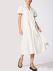 Woman in a classy white tiered midi shirtdress with puff sleeves, holding the flowing skirt as it swings, styled with tan sandals.