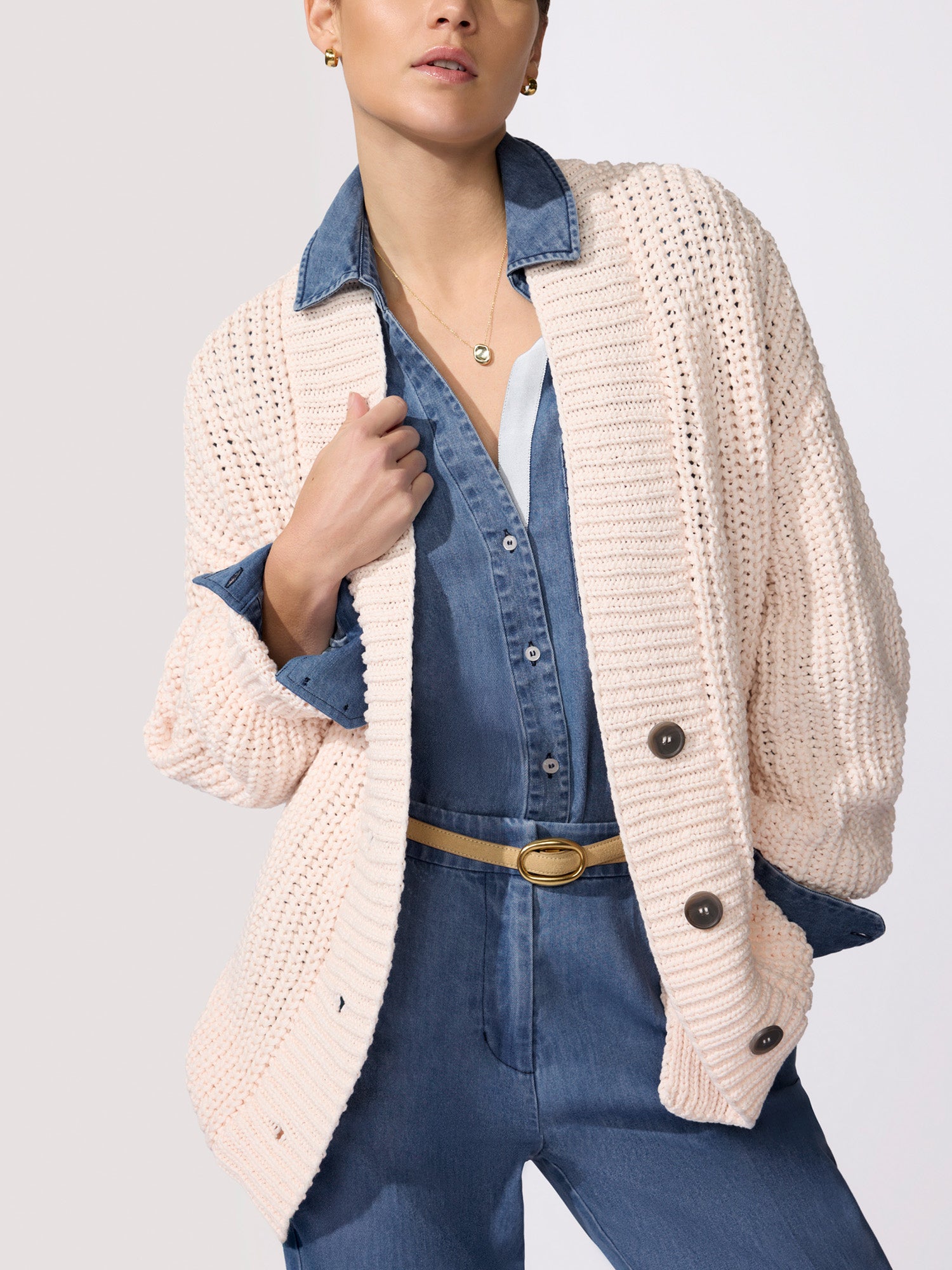 Classy denim outfit with a medium-wash button-front shirt layered under a blush pink chunky knit open cardigan with tan belt.
