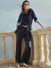 Woman wearing a navy knit sweater over a striped shirt with a tan belt, leaning on a stone balcony railing