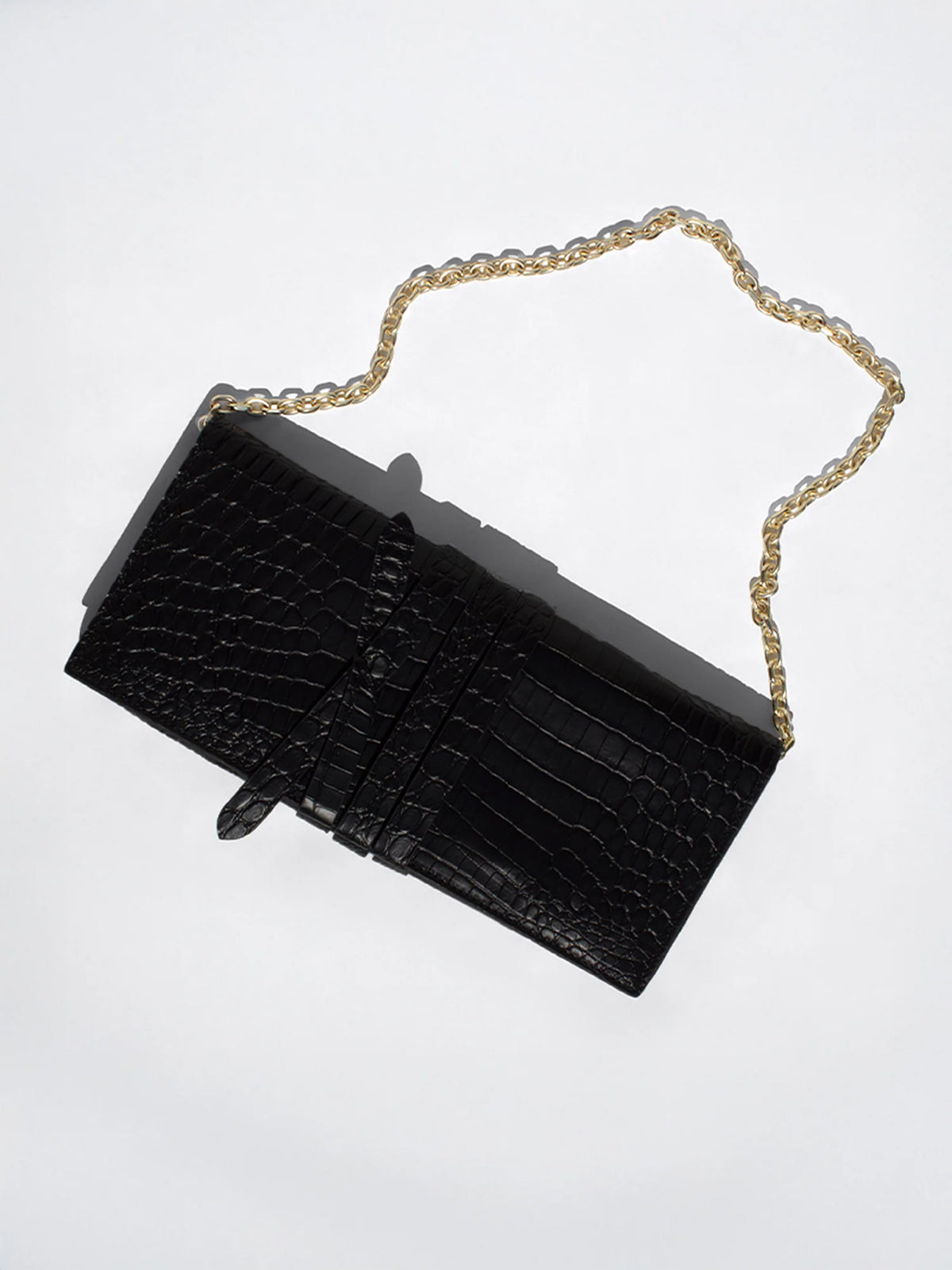 Black crocodile leather shoulder pochette with a gold chain strap, laid flat on a light gray background