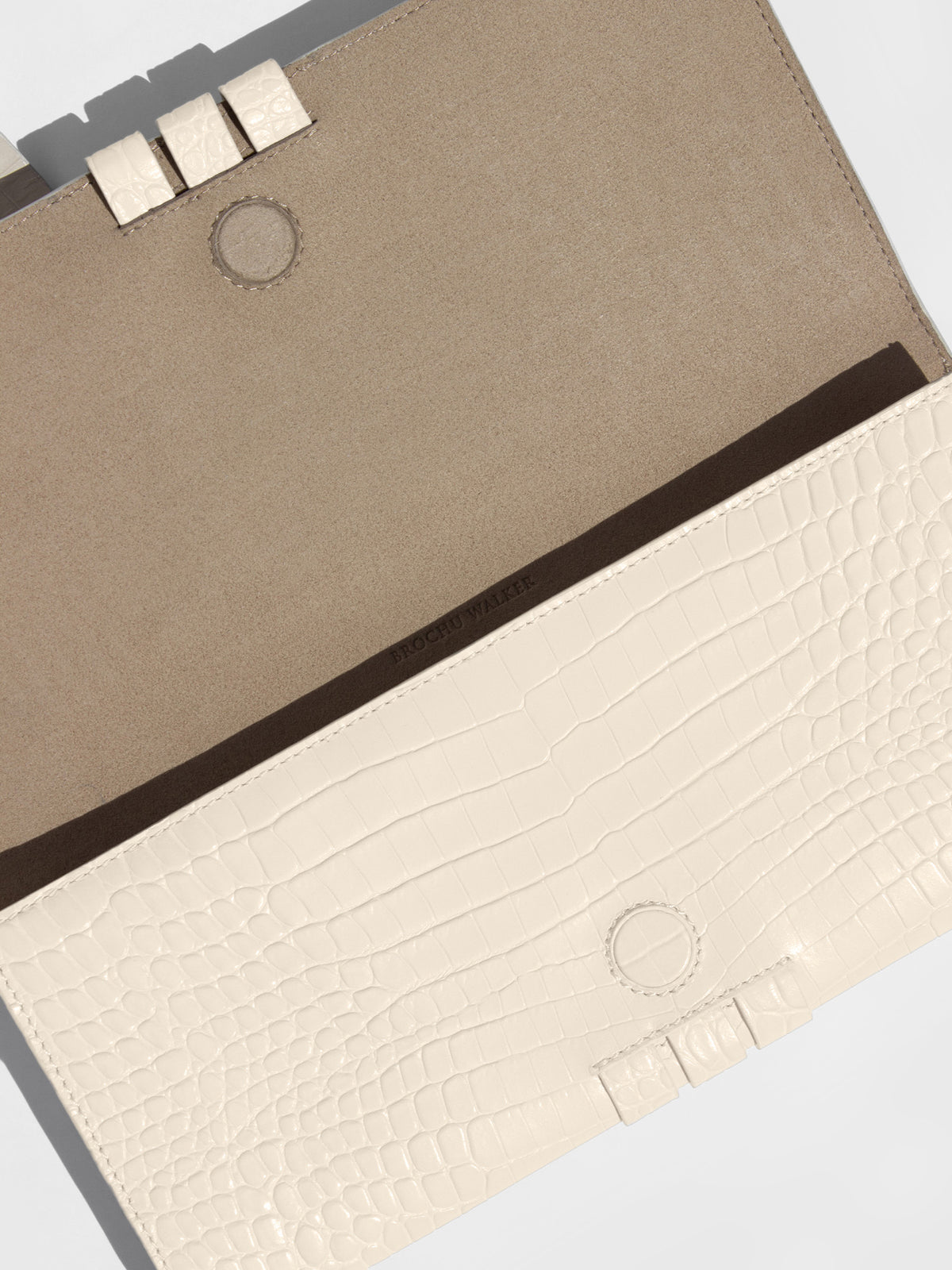 Ivory croc-embossed clutch bag open to reveal its taupe suede lining and snap closure