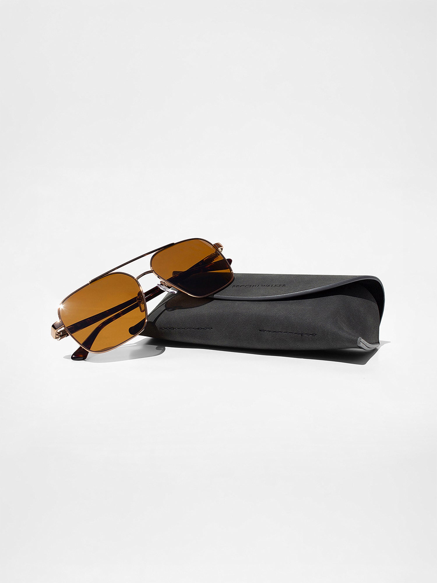 Gold-frame aviator sunglasses with amber lenses resting against a gray suede sunglasses case
