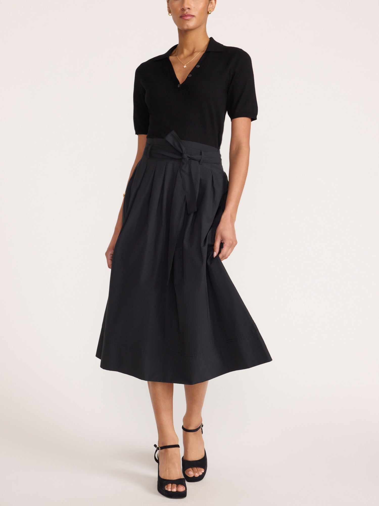 Isola dress in black onyx, full-length front view with pleated tie-waist midi skirt and strappy heels
