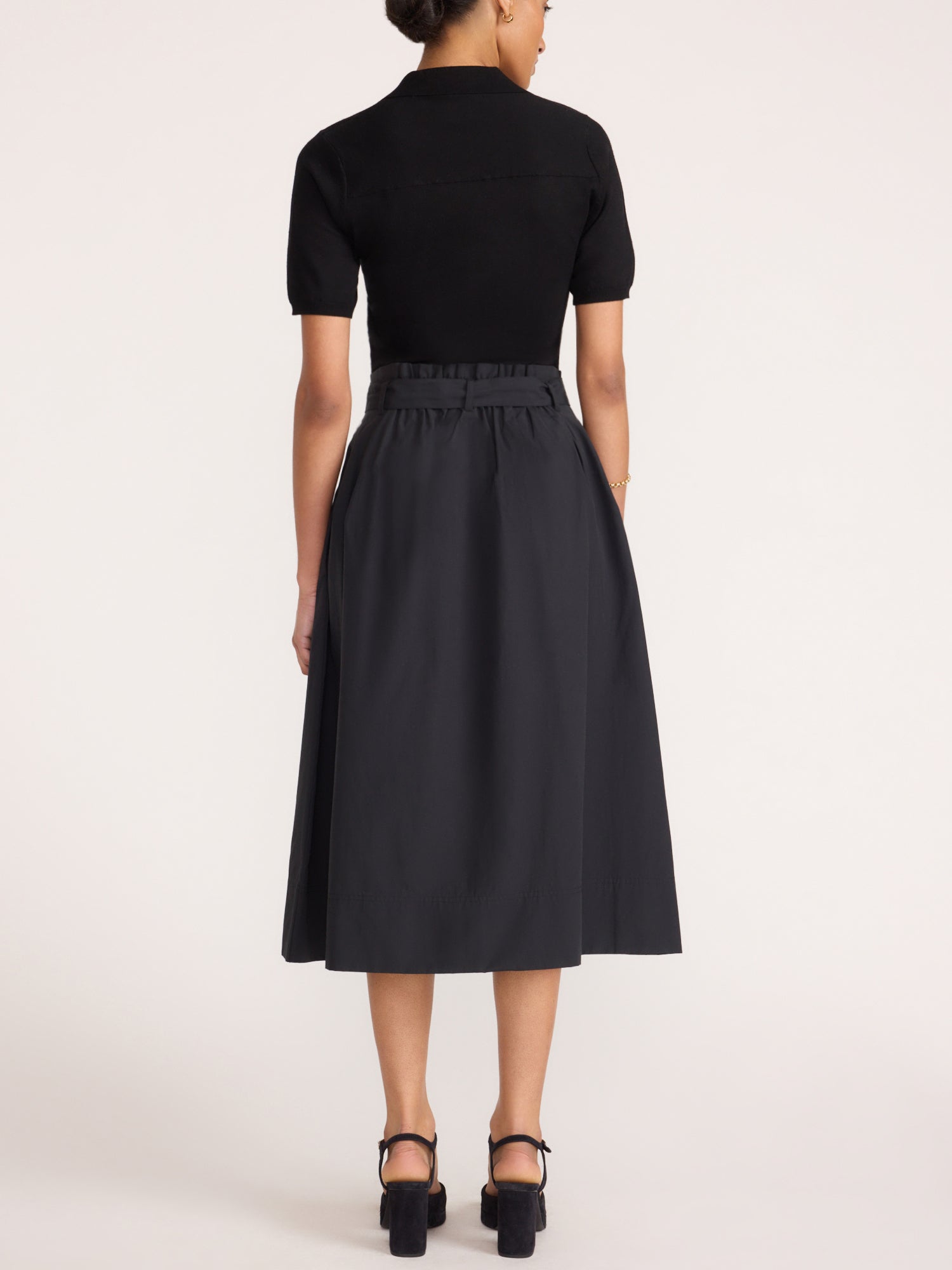 Isola dress in black onyx, back view with pleated midi skirt and platform heels