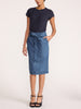 Women's denim skirt in a light-wash midi length with a self-tie waist bow, side pocket, and topstitched hem paired with a navy tee and black heels.