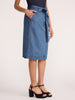 Women's denim skirt in light-wash with a self-tie waist, side pocket, and topstitched hem shown from the side with black platform heels.