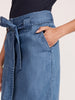 Women's denim skirt close-up showing a light-wash self-tie bow waistband, side seam pocket detail, and hand tucked into front pocket.