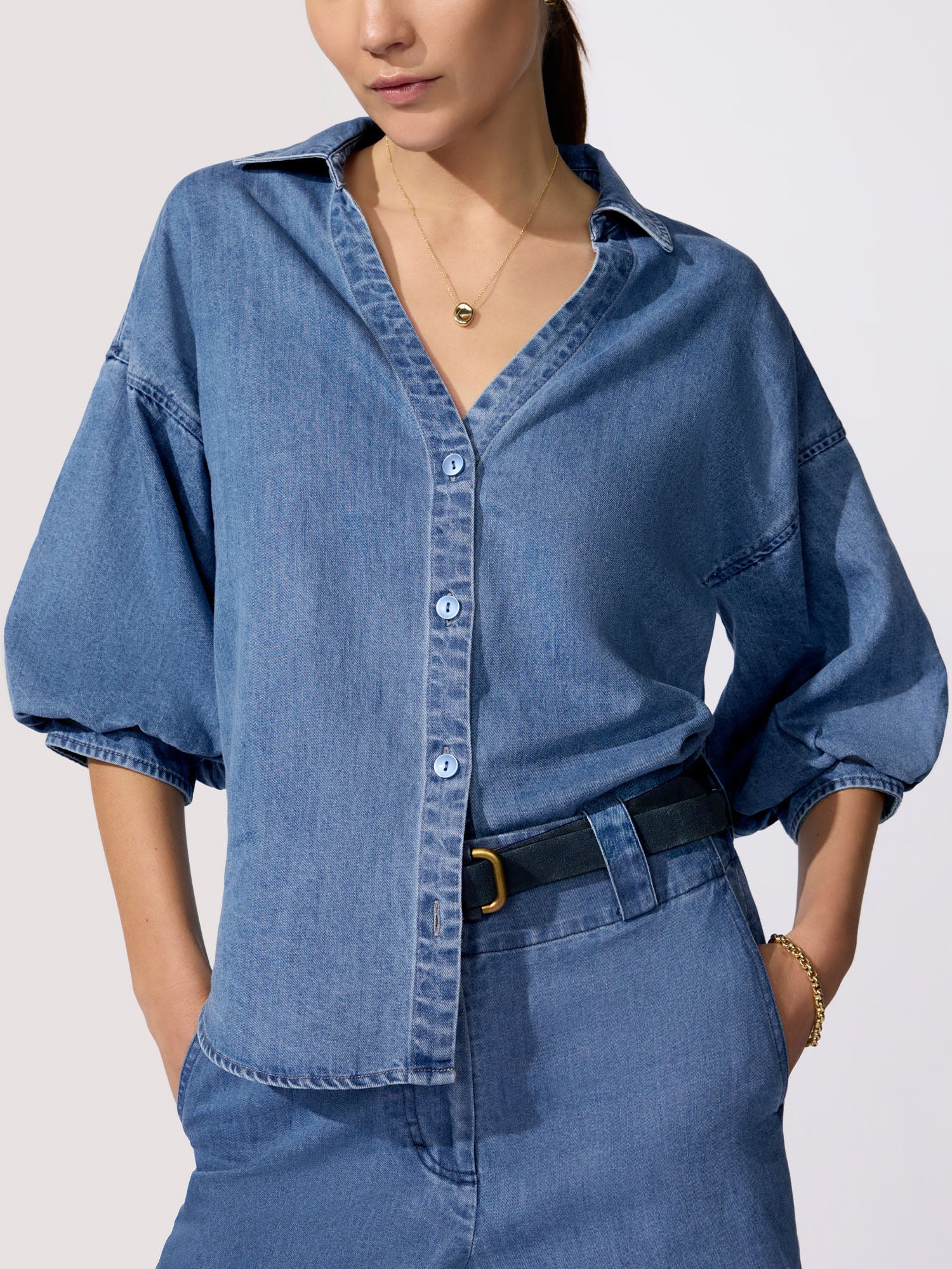 Women's denim outfit featuring a medium-wash oversized shirt with balloon sleeves, V-neckline, and black belt paired with denim trousers.