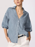 Ladies denim shirt in medium-wash chambray with balloon sleeves, open V-neckline, and button-front styled over white trousers with a dark belt.