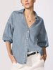 Ladies denim shirt in medium-wash chambray with balloon sleeves, open V-neckline, and button-front styled over white trousers with a dark belt.