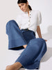 Classy white top with a mock neck, puff sleeves, and snap buttons worn seated with wide-leg medium-wash denim trousers and a dark belt.