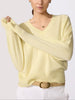 Classy women's sweater in pale yellow cashmere with a V-neckline, dolman sleeves, and ribbed hem shown in a close-up upper-body view.
