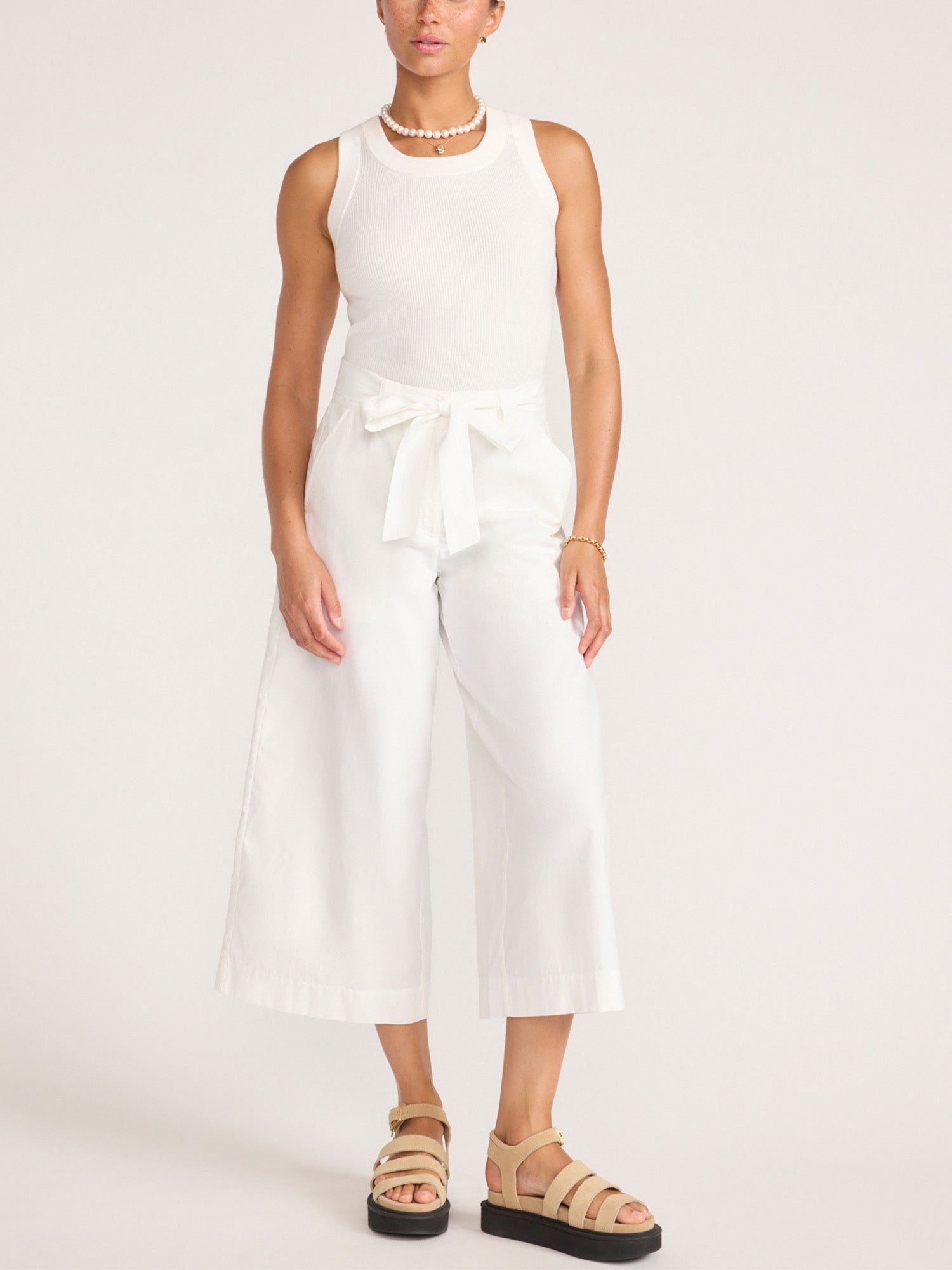 Full-length look featuring the white Leo Tank with ivory wide-leg cropped pants and tan platform sandals.