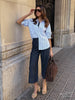 Elegant classy outfit with a blue striped oversized shirt tucked into dark-wash wide-leg cropped trousers with a brown tote bag on a city street.