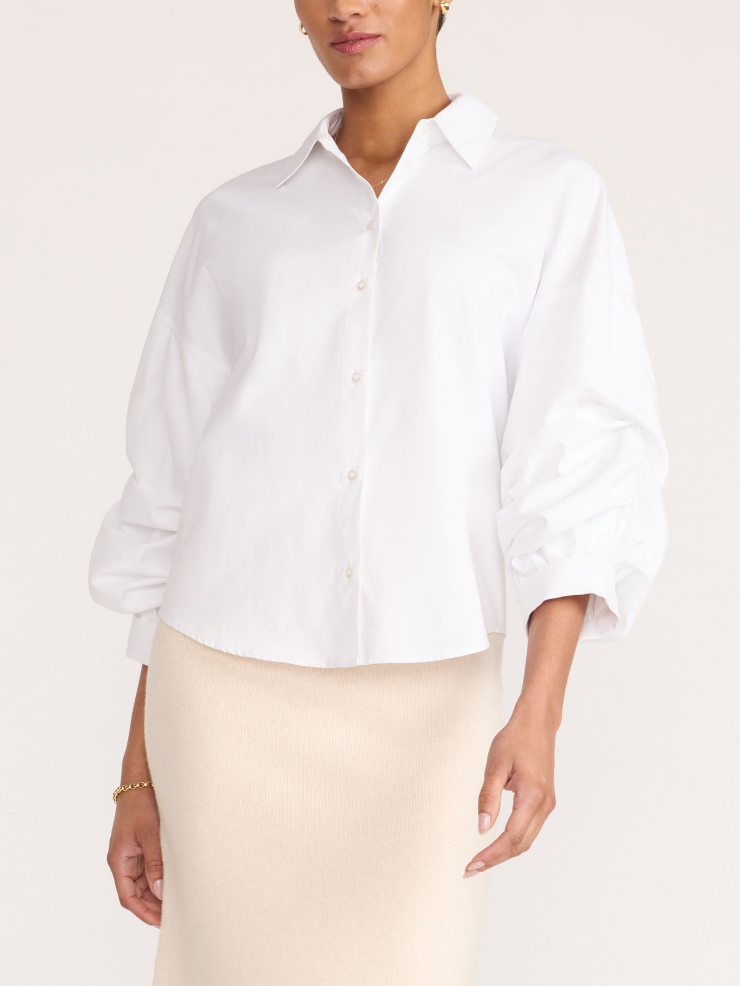 White button-up shirt with voluminous sleeves, styled with a cream-colored skirt, studio portrait
