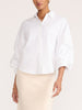 White button-up shirt with voluminous sleeves, styled with a cream-colored skirt, studio portrait