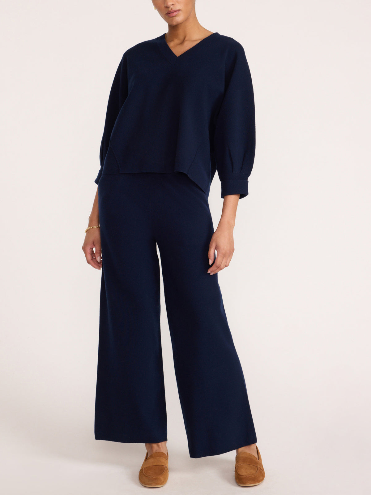 Women's navy blue two-piece knit set with a cropped V-neck top and wide-leg trousers, paired with suede loafers