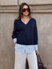 Classy women's sweater in a navy V-neck knit layered over a blue striped collared shirt with cream wide-leg trousers and a brown bag outdoors.