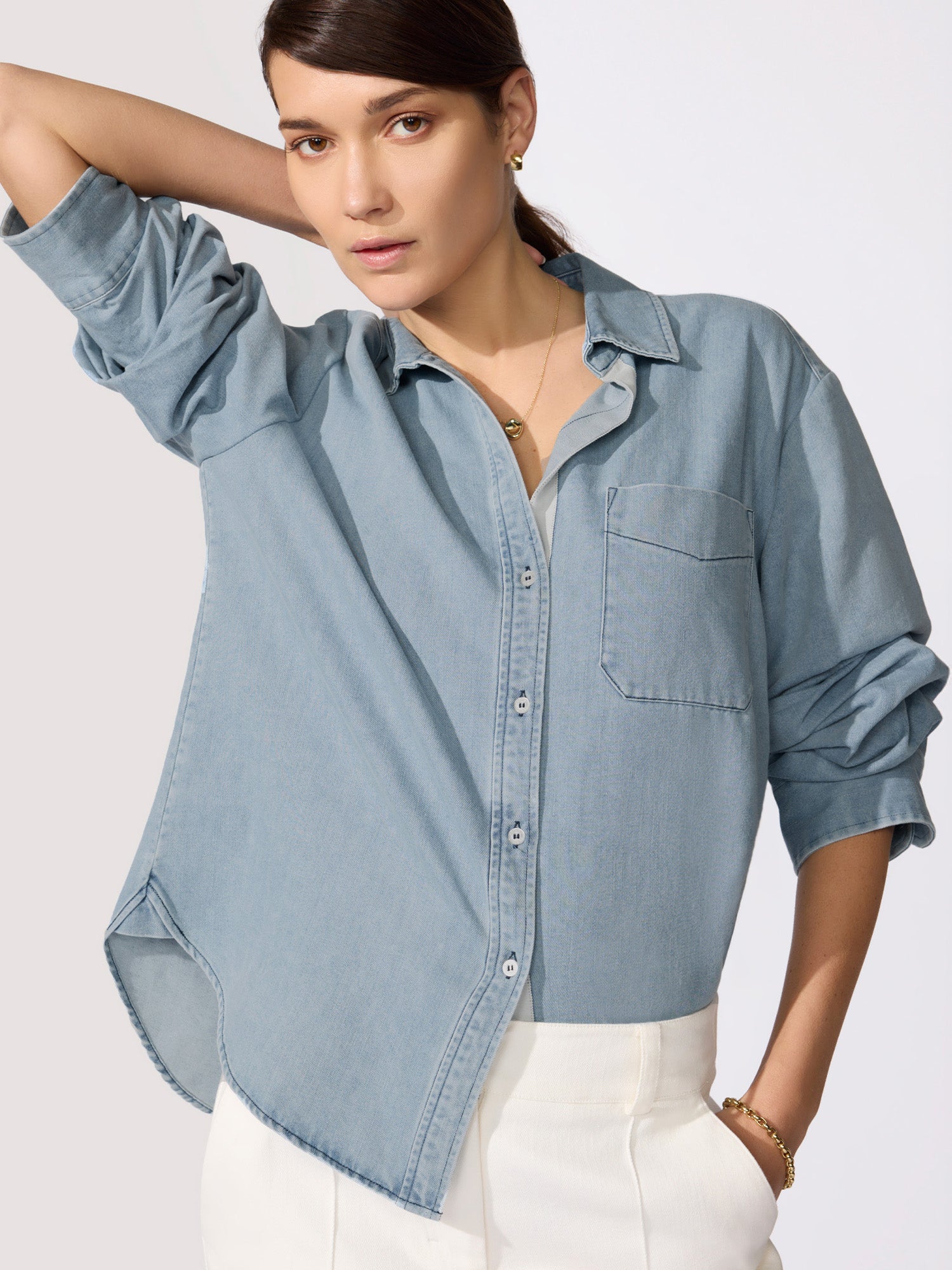 Ladies denim shirt in light-wash chambray with an open collar, chest pocket, and rolled sleeves styled with white pants.