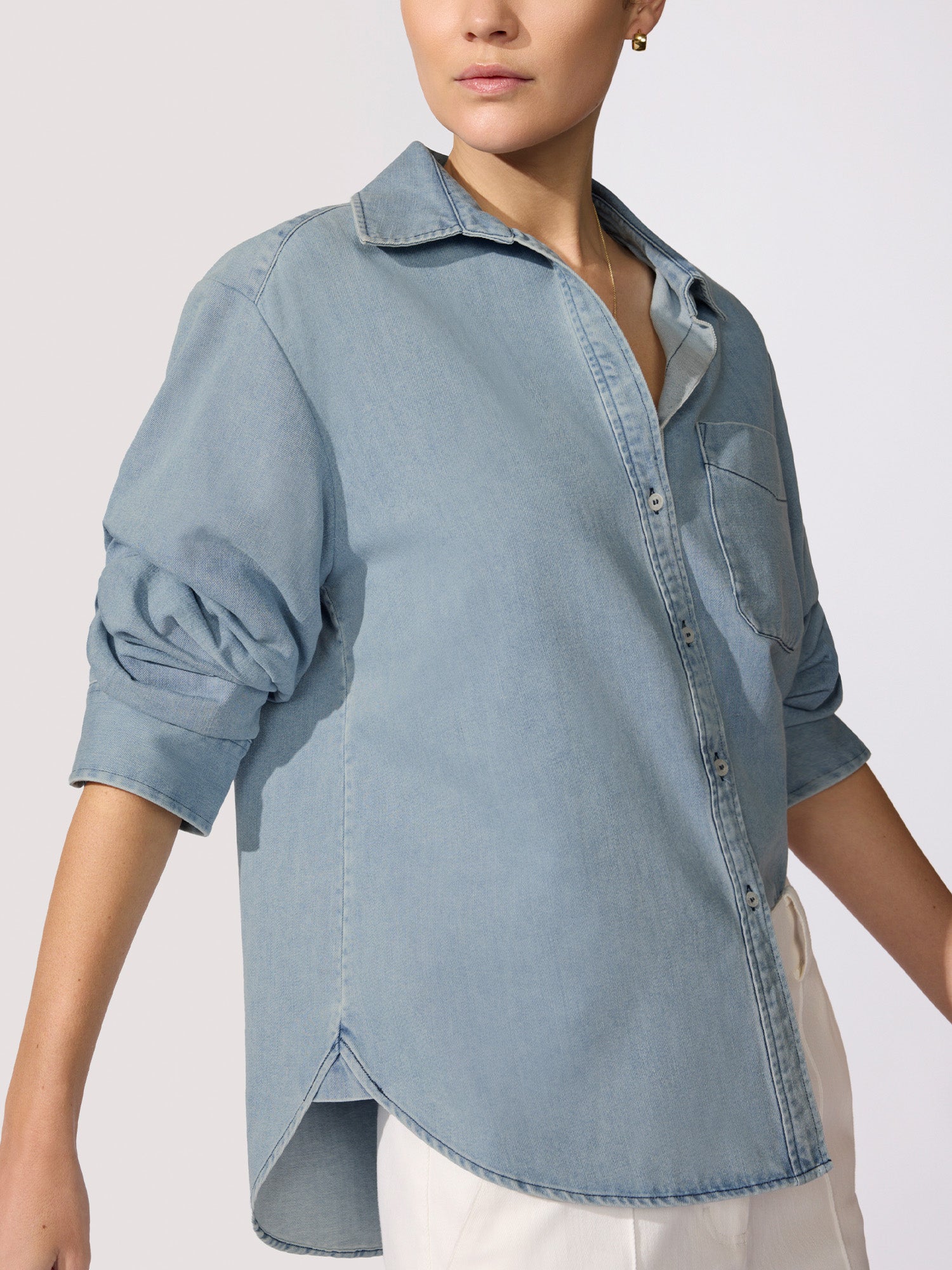 Denim shirt for women in light-wash chambray with a relaxed fit, chest pocket, and curved hem shown from the side.