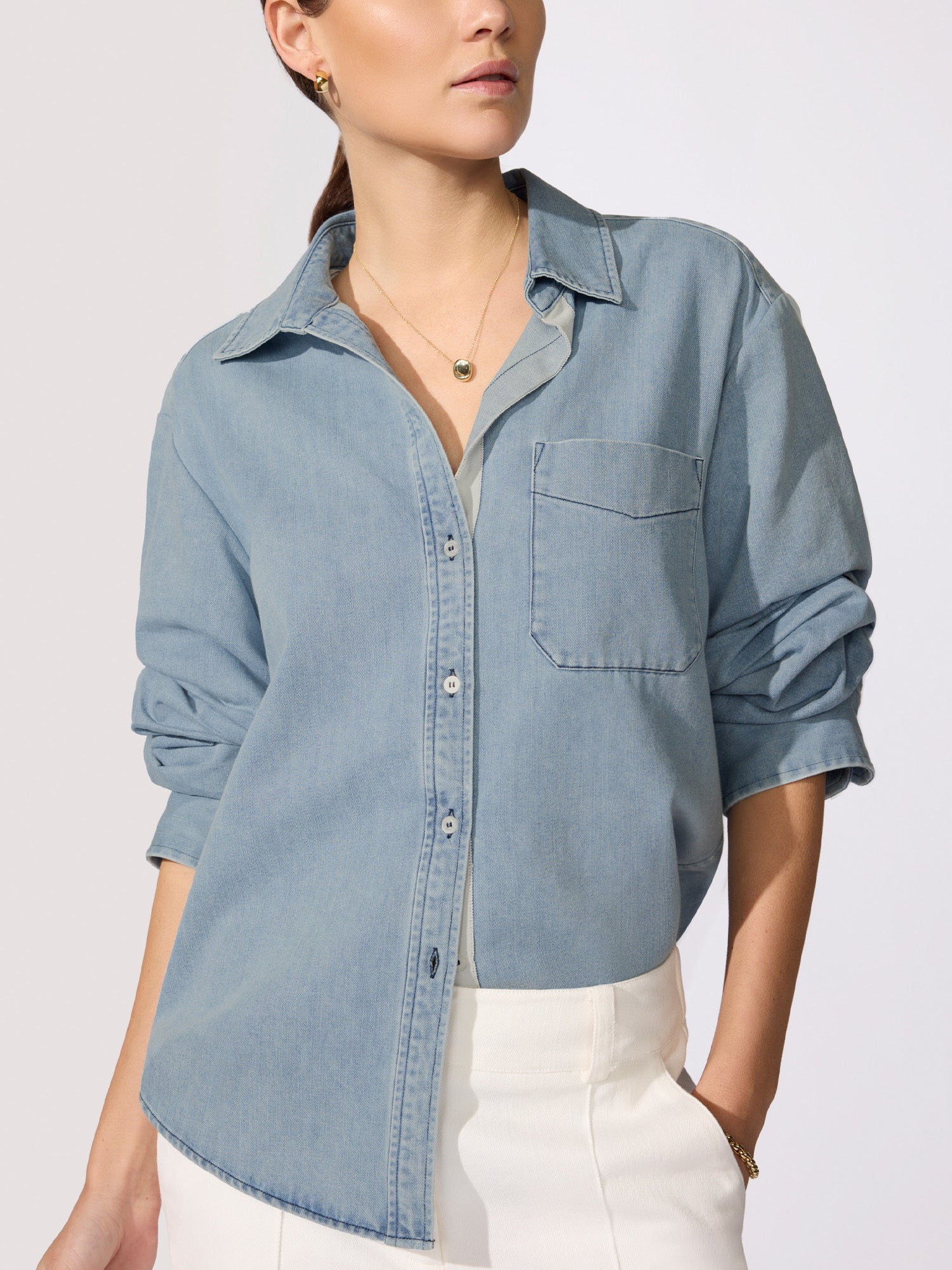 Woman wearing a light blue denim button-up shirt with rolled sleeves and white pants