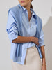 Women's blue button up shirt styled with a matching sweater draped over the shoulders and a beige skirt.