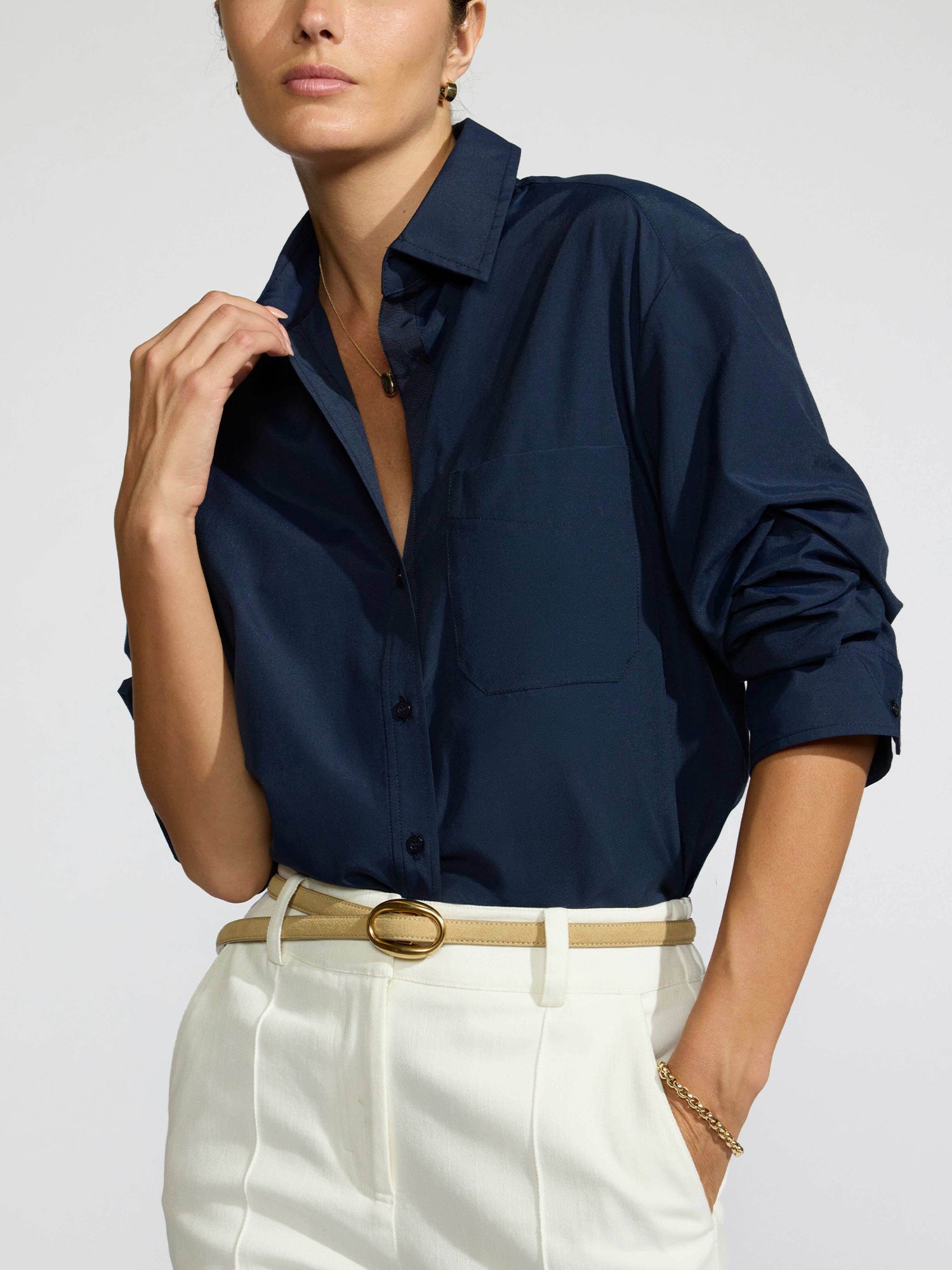 Model wearing the Pia shirt in navy tucked into white trousers with a tan leather belt