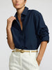 Model wearing the Pia shirt in navy tucked into white trousers with a tan leather belt