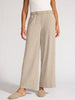 Woman wearing elegant sand-colored wide-leg linen dress pants with an elastic waist and cuffed hem, styled with ivory slip-on flats.