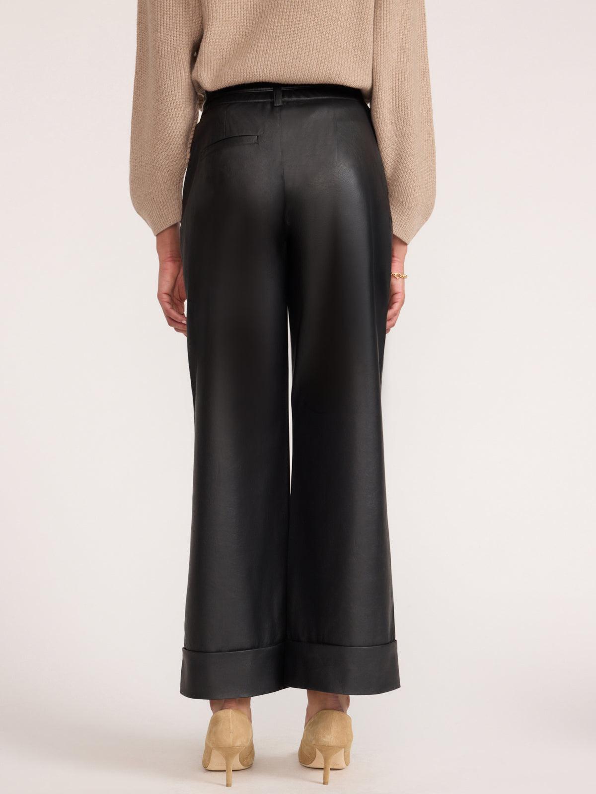 Women's black wide-leg vegan leather trousers, back view styled with a beige knit sweater and heels