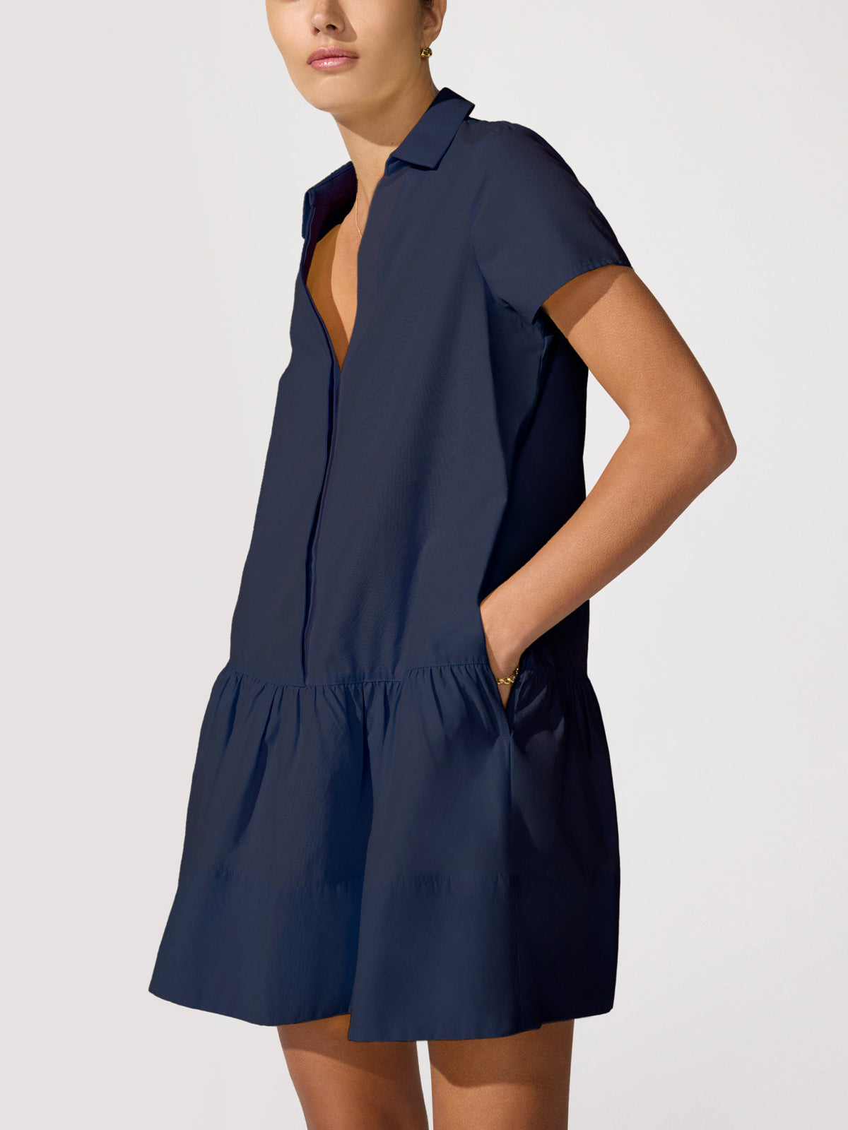 Woman wearing a navy tiered shirt dress with short sleeves and a button-front placket, hand tucked in the pocket