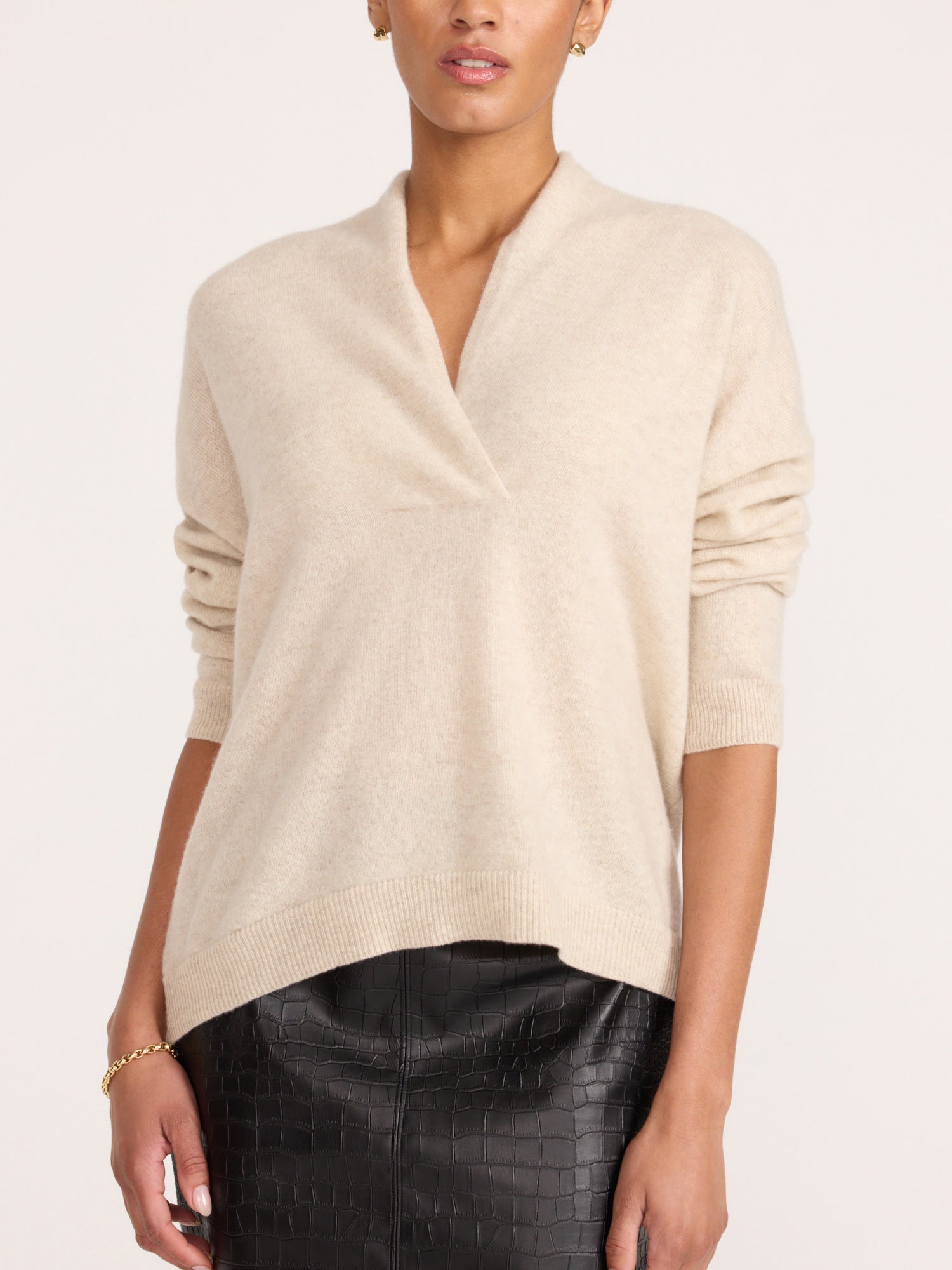Front view of a woman wearing the Brochu Walker Siena Wrap Neck Cashmere Pullover in Stone Melange, a cream sweater with a split V-neck, paired with dark textured pants.