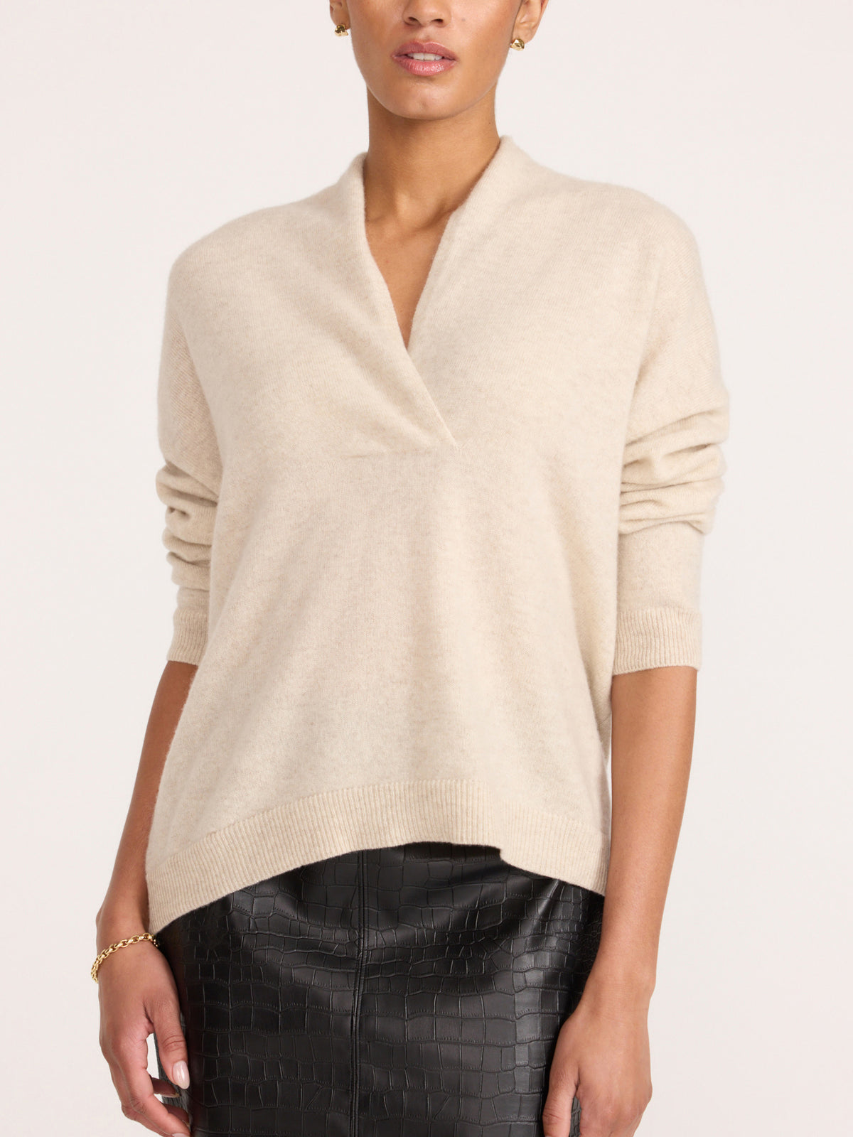 Front view of a woman wearing the Brochu Walker Siena Wrap Neck Cashmere Pullover in Stone Melange, a cream sweater with a split V-neck, paired with dark textured pants.
