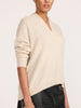 Side view of a woman wearing the Brochu Walker Siena Wrap Neck Cashmere Pullover in Stone Melange, a cream V-neck sweater paired with dark textured pants.