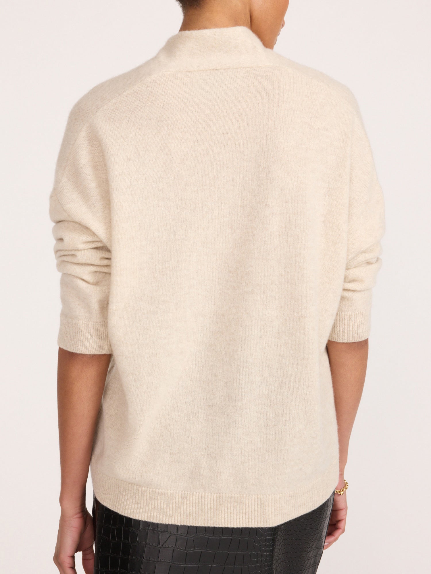 Back view of a woman wearing the Brochu Walker Siena Wrap Neck Cashmere Pullover in Stone Melange, a cream mock-neck sweater paired with dark textured pants.