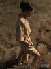 Woman walking through a dry grass field wearing a beige linen shirt and shorts