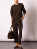 Woman wearing a matching dark chocolate brown crewneck sweatshirt and wide-leg jogger set, styled with a suede tote and mary jane flats.
