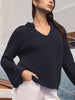 Woman wearing The Aria Popover, a navy waffle-knit V-neck sweater with flared cuffs, standing on a sailboat