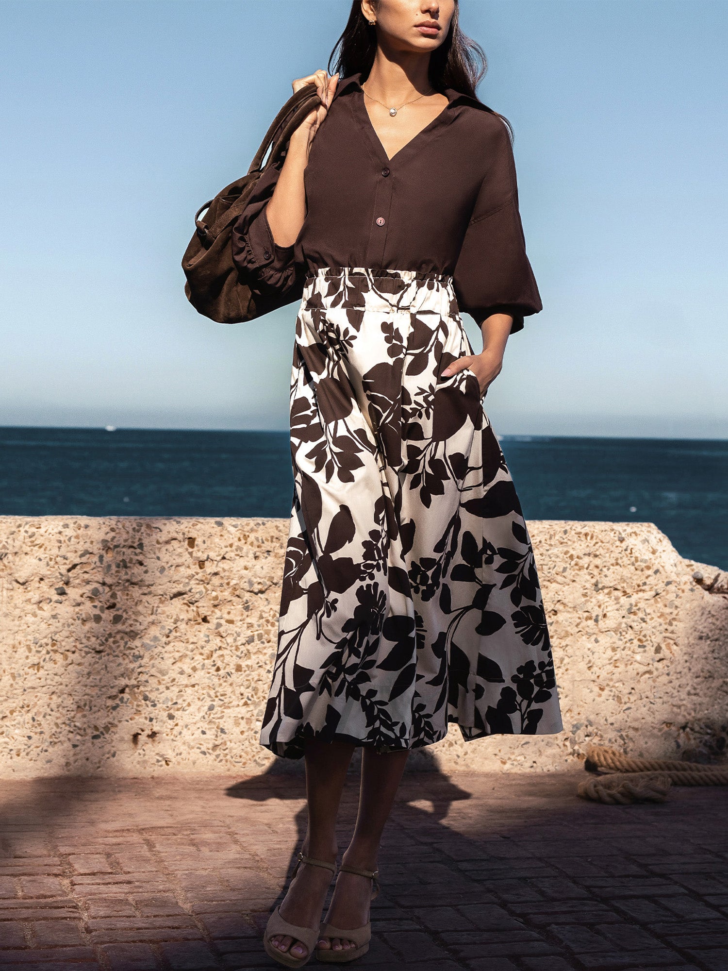 Woman wearing The Edda Printed Skirt, a black-and-white floral midi skirt, standing by the sea