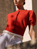 Woman wearing The Havana Cardigan in red, a short-sleeve knit cardigan, against a stone wall