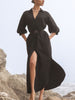 Woman wearing The Kate Maxi Dress in black, a belted V-neck maxi dress with puff sleeves, on a rocky beach